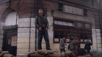 Movie still from “Empire of the Sun” (1987), directed by Steven Spielberg – A man standing on top of a pile of sand bags; Wide shot, Low angle