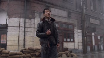 Movie still from “Empire of the Sun” (1987), directed by Steven Spielberg – A man standing in front of a pile of sandbags in front of a building; Medium shot, Low angle