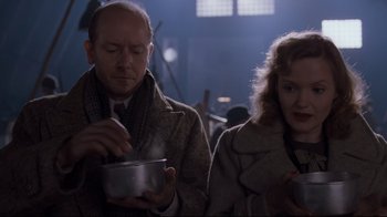 Movie still from “Empire of the Sun” (1987), directed by Steven Spielberg – A man and a woman are holding a bowl of food; Medium shot, Low angle