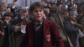 Movie still from “Empire of the Sun” (1987), directed by Steven Spielberg – A young boy in a red jacket is in front of a group of men; Close Up shot, Low angle