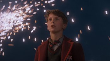 Movie still from “Empire of the Sun” (1987), directed by Steven Spielberg – A young boy in a red jacket looking up at fireworks in the background; Medium shot, Low angle