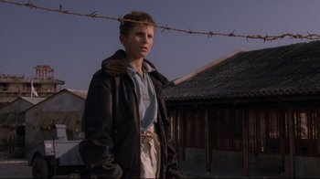 Movie still from “Empire of the Sun” (1987), directed by Steven Spielberg – A young man standing in front of barbed wire; Medium shot, Low angle