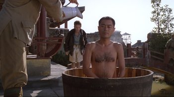 Movie still from “Empire of the Sun” (1987), directed by Steven Spielberg – A man sitting in a wooden tub in front of another man; Medium shot, Low angle