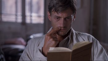 Movie still from “Empire of the Sun” (1987), directed by Steven Spielberg – A man reading a book while sitting in a chair; Close Up shot, Low angle