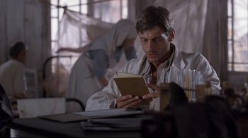 Movie still from “Empire of the Sun” (1987), directed by Steven Spielberg – A man sitting at a table reading a book; Medium shot, Low angle