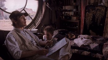 Movie still from “Empire of the Sun” (1987), directed by Steven Spielberg – A man and a boy are sitting in a room together; Medium shot, Over the shoulder angle
