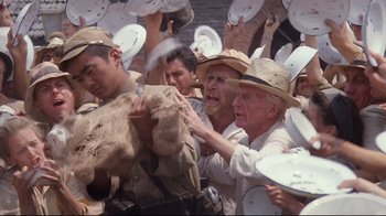 Movie still from “Empire of the Sun” (1987), directed by Steven Spielberg – A group of men in hats and some are holding plates; Medium shot, High angle