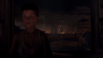 Movie still from “Empire of the Sun” (1987), directed by Steven Spielberg – A young boy is standing in a dark room; Close Up shot, High angle