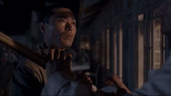 Movie still from “Empire of the Sun” (1987), directed by Steven Spielberg – A man standing in a room with a microphone; Close Up shot, Over the shoulder angle