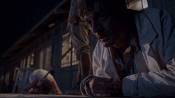 Movie still from “Empire of the Sun” (1987), directed by Steven Spielberg – A man in white shirt and brown tie laying on the ground; Medium shot, Low angle
