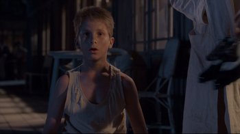 Movie still from “Empire of the Sun” (1987), directed by Steven Spielberg – A young boy in a tank top looking at the camera; Medium shot, Low angle