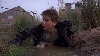 Movie still from “Empire of the Sun” (1987), directed by Steven Spielberg – A young boy in the water with barbed wire around his neck; Medium shot, High angle