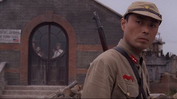 Movie still from “Empire of the Sun” (1987), directed by Steven Spielberg – A man with a rifle standing in front of a brick building; Close Up shot, Low angle