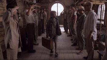 Movie still from “Empire of the Sun” (1987), directed by Steven Spielberg – A group of men standing around a woman carrying a suitcase; Wide shot, Low angle