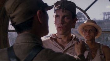 Movie still from “Empire of the Sun” (1987), directed by Steven Spielberg – A man with a hat on and two other men standing next to him; Close Up shot, Over the shoulder angle