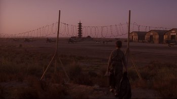 Movie still from “Empire of the Sun” (1987), directed by Steven Spielberg – A person standing on a dirt road near a barbed wire fence; Extreme Wide shot, Low angle