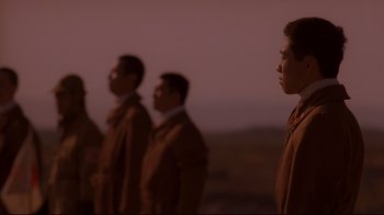 Movie still from “Empire of the Sun” (1987), directed by Steven Spielberg – A group of men standing next to each other in front of a sunset; Medium shot, Low angle