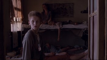 Movie still from “Empire of the Sun” (1987), directed by Steven Spielberg – A young boy standing in a room next to bunk beds; Medium shot, High angle