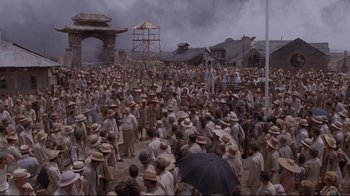 Movie still from “Empire of the Sun” (1987), directed by Steven Spielberg – A crowd of people standing in front of a building; Extreme Wide shot, High angle