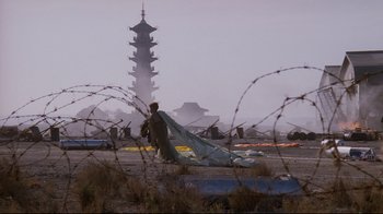 Movie still from “Empire of the Sun” (1987), directed by Steven Spielberg – A man standing on top of a field near barbed wire; Extreme Wide shot, Low angle