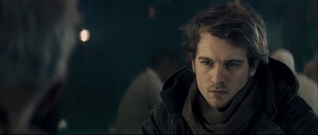 Movie still from “Empire of the Wolves” (2005), directed by Chris Nahon – A man with a beard and a jacket on looking at the camera; Close Up shot, Over the shoulder angle