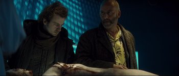 Movie still from “Empire of the Wolves” (2005), directed by Chris Nahon – Two men are looking at a dead body in a dark room; Close Up shot, Low angle