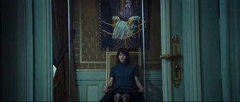 Movie still from “Empire of the Wolves” (2005), directed by Chris Nahon – A woman sitting in a chair in front of a painting; Medium shot, Low angle