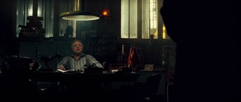 Movie still from “Empire of the Wolves” (2005), directed by Chris Nahon – An older man sitting at a desk in a dark room; Medium shot, Over the shoulder angle