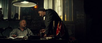 Movie still from “Empire of the Wolves” (2005), directed by Chris Nahon – A man standing at a table in front of a window; Medium shot, Over the shoulder angle