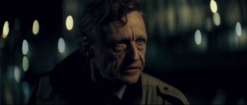 Movie still from “Empire of the Wolves” (2005), directed by Chris Nahon – An old man with a goatee looking at the camera; Close Up shot, Over the shoulder angle