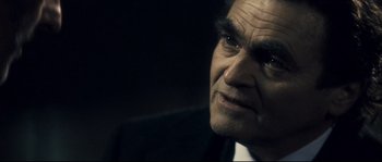 Movie still from “Empire of the Wolves” (2005), directed by Chris Nahon – An older man in a black suit looking to his left; Close Up shot, Over the shoulder angle
