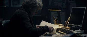 Movie still from “Empire of the Wolves” (2005), directed by Chris Nahon – A person sitting at a desk with a computer; Medium shot, High angle