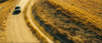 Movie still from “Empire of the Wolves” (2005), directed by Chris Nahon – An aerial view of a dirt road in the middle of a field; Extreme Wide shot, Overhead angle