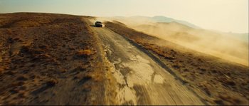Movie still from “Empire of the Wolves” (2005), directed by Chris Nahon – A car driving down a dirt road in the desert; Extreme Wide shot, High angle