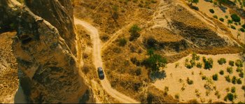 Movie still from “Empire of the Wolves” (2005), directed by Chris Nahon – An aerial view of a car driving down a dirt road; Extreme Wide shot, Overhead angle