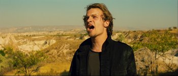Movie still from “Empire of the Wolves” (2005), directed by Chris Nahon – A man with long blonde hair is singing; Close Up shot, Low angle