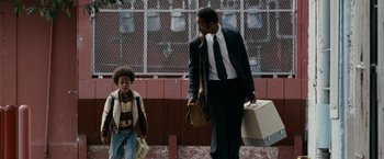 Movie still from “The Pursuit of Happyness” (2006), created by Frank Darabont – A man in a suit and tie walking next to a young boy; Medium shot, Low angle