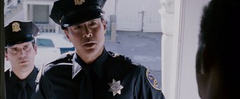 Movie still from “The Pursuit of Happyness” (2006), created by Frank Darabont – A police officer in uniform standing next to a white pillar; Close Up shot, Low angle