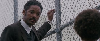Movie still from “The Pursuit of Happyness” (2006), created by Frank Darabont – A man in a suit and tie standing next to a chain link fence; Close Up shot, Low angle