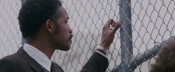 Movie still from “The Pursuit of Happyness” (2006), created by Frank Darabont – A man in a suit is looking over a chain link fence; Close Up shot, Low angle