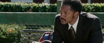 Movie still from “The Pursuit of Happyness” (2006), created by Frank Darabont – A man sitting on a park bench wearing a suit and tie; Close Up shot, Over the shoulder angle