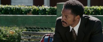 Movie still from “The Pursuit of Happyness” (2006), created by Frank Darabont – A man in a suit and tie sitting on top of a wooden bench; Close Up shot, Over the shoulder angle