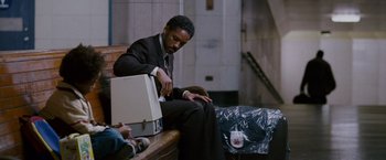 Movie still from “The Pursuit of Happyness” (2006), created by Frank Darabont – A man in a suit sitting on a bench; Medium shot, Low angle
