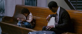 Movie still from “The Pursuit of Happyness” (2006), created by Frank Darabont – Two people sitting on a wooden bench one of which is using a cell phone; Medium shot, High angle