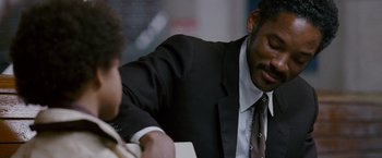 Movie still from “The Pursuit of Happyness” (2006), created by Frank Darabont – A man wearing a suit and tie sitting at a table; Close Up shot, Over the shoulder angle