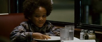 Movie still from “The Pursuit of Happyness” (2006), created by Frank Darabont – A young boy sitting at a table eating a piece of pizza; Close Up shot, Over the shoulder angle