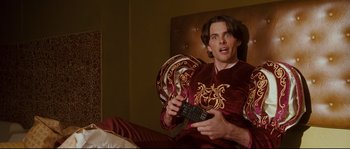 Movie still from “Enchanted” (2007), directed by Kevin Lima – A man sitting on a bed holding a remote control; Medium shot, Low angle