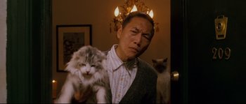 Movie still from “Enchanted” (2007), directed by Kevin Lima – A man holding a cat in a room with a chandelier; Medium shot, Low angle