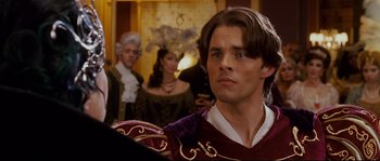 Movie still from “Enchanted” (2007), directed by Kevin Lima – A man in a red and purple outfit standing in front of a group of people; Close Up shot, Over the shoulder angle