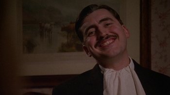 Movie still from “Enchanted April” (1991), directed by Mike Newell – A man in a suit smiling for the camera; Close Up shot, Low angle